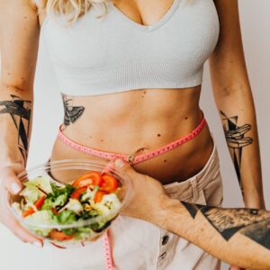 Fit woman measuring waist while holding a healthy salad bowl