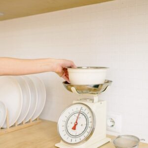 A hand placing a bowl on a retro kitchen scale in a modern kitchen setting.