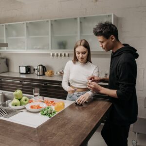 Young couple managing diabetes with glucometer while preparing a healthy meal in a modern kitchen.