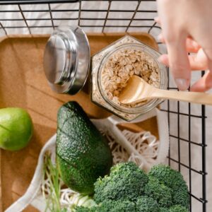 A metal basket with fresh vegetables, avocado, lime, and oats arranged in a flat lay style.
